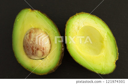 Ripe halved avocado with bone on black stone board 121974301