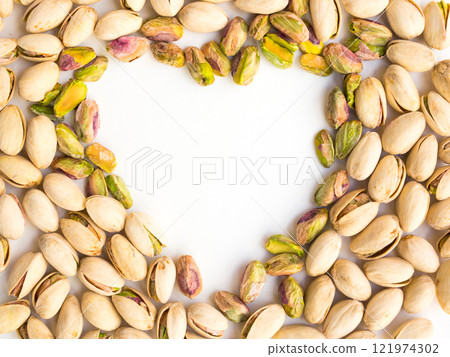 Roasted salted pistachio nuts on a white background and place for inscription in form of heart 121974302