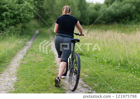 Woman cycling on a trail through green countryside. Enjoy the fresh air and outdoor fitness. Woman cycling on a trail through green countryside. Enjoy the fresh air and outdoor fitness. 121975798