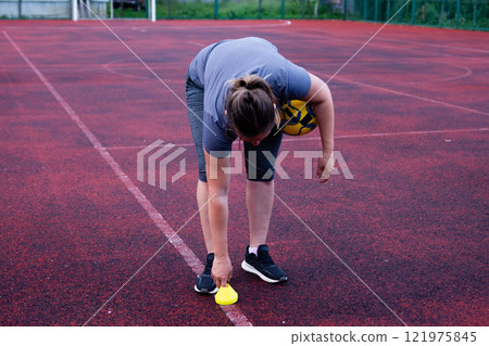 Woman placing a marker cone on a sports field, preparing for practice or a game. 121975845