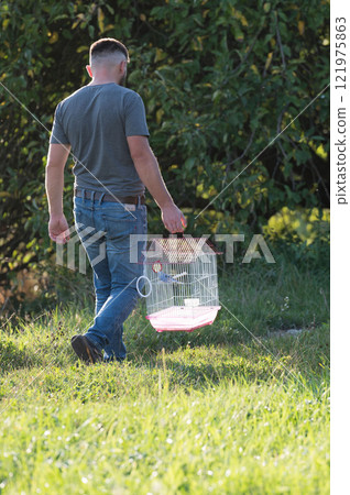 Man carrying a birdcage in a grassy field. Man carrying a birdcage in a grassy field. 121975863