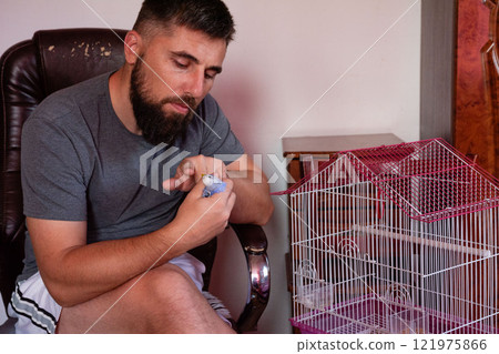 Man gently holding a small blue bird, near its cage. A moment of quiet connection. Man gently holding a small blue bird, near its cage. A moment of quiet connection. 121975866