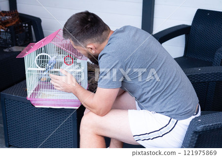 Man looking at his pet bird in a cage outdoors. Man looking at his pet bird in a cage outdoors. 121975869