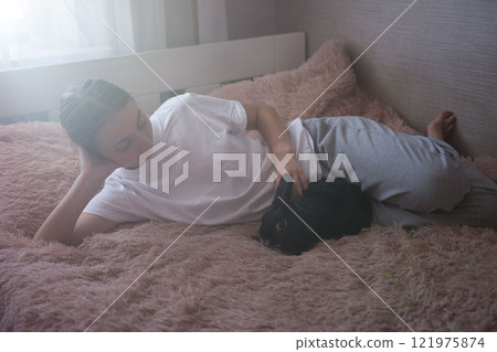 Woman relaxing in bed with pet rabbit. Peaceful morning scene. 121975874