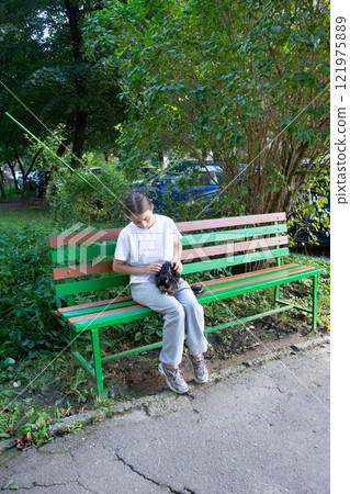Girl sitting on a park bench petting a small animal. 121975889