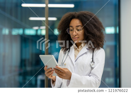 Serious female doctor focused and thinking using tablet computer, female doctor in white medical coat working inside clinic office. Serious female doctor focused and thinking using tablet computer, female doctor in white medical coat working inside clinic office. 121976022
