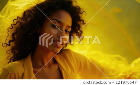 Woman with curly hair poses elegantly with yellow fabric in a vibrant setting during golden hour 121976547