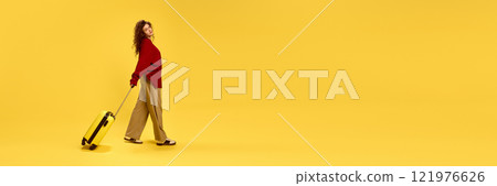 Banner. Young beautiful woman dressed casually, walking with luggage against sunny yellow background with negative space to insert text. 121976626
