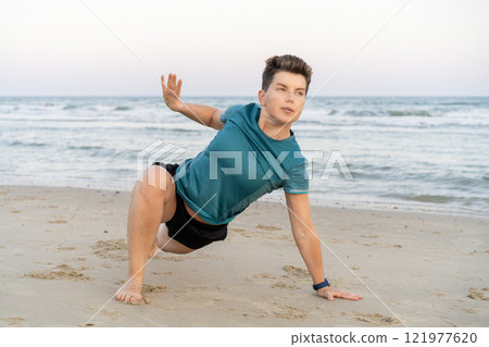 Sporty woman is engaged in animal flow gymnastics outdoors on sea beach. Female trains with Animal Flow workout to elevate her body weight workout. Innovative animal instinct fitness sport movement. Sporty woman is engaged in animal flow gymnastics outdoors on sea beach. Female trains with Animal Flow workout to elevate her body weight workout. Innovative animal instinct fitness sport movement. 121977620