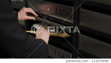 Close-up woman is opening her mailbox inside a cluster of mailboxes for her apartment. Mail shipping concept. Close-up woman is opening her mailbox inside a cluster of mailboxes for her apartment. Mail shipping concept. 121978099
