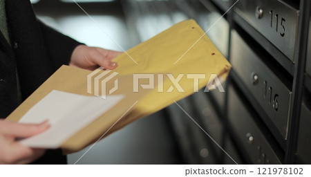 Close up woman is opening her mailbox inside a cluster of mailboxes for her apartment. Payment notification letter. Mail shipping concept. 121978102