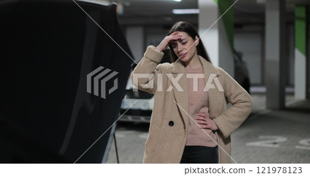 Young woman near a broken car in the parking lot with the hood open. 121978123