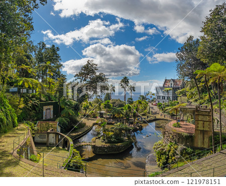 A picturesque Monte Palace tropical garden in Funchal on Madeira. Reflective pond surrounded by lush, vibrant greenery and architectural structures 121978151