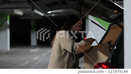 Young woman walks through the parking lot of shopping center to car. Puts paper bags with purchases. Shopping, sale, discounts in stores. Young woman walks through the parking lot of shopping center to car. Puts paper bags with purchases. Shopping, sale, discounts in stores. 121978194