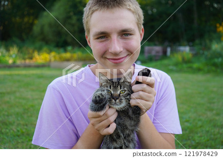 A teenager plays with a cat in the fresh air 121978429