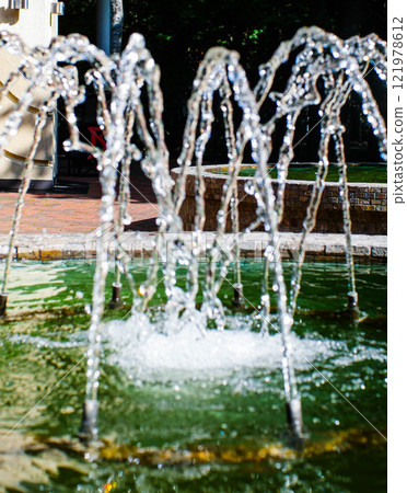 Vertical jets of water from the fountain. Close-up view. Jets flowing out of the fountain. Summer urban landscape 121978612
