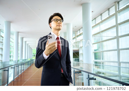穿著西裝的商人拿著智慧型手機沿著走廊走 121978702