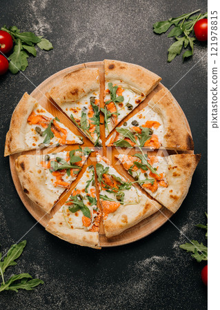 Sliced gourmet pizza with smoked salmon, arugula, and capers on a wooden board for a stylish feast 121978815