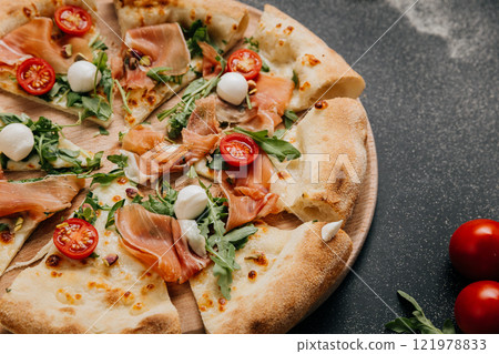 Delicious prosciutto and arugula pizza with cherry tomatoes and mozzarella on a wooden platter 121978833