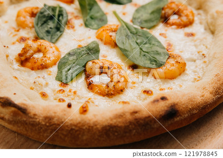 Gourmet shrimp pizza topped with fresh spinach leaves on a golden crust served on a wooden platter 121978845