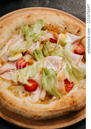 Gourmet salad pizza with lettuce, cherry tomatoes, turkey slices, and cheese on a wooden plate Gourmet salad pizza with lettuce, cherry tomatoes, turkey slices, and cheese on a wooden plate 121978847