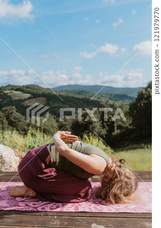 Young woman doing yoga outdoors against hilly landscape 121979770