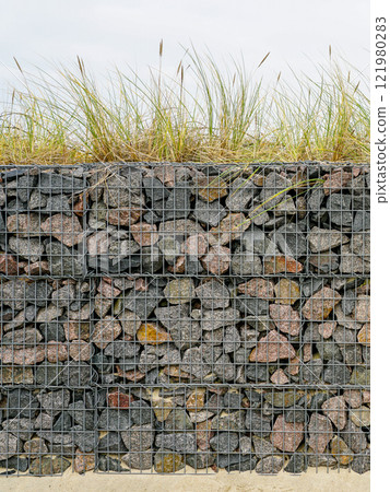 Gabion fence wall from steel mesh filled with granite stones, modern seaside environmental object 121980283