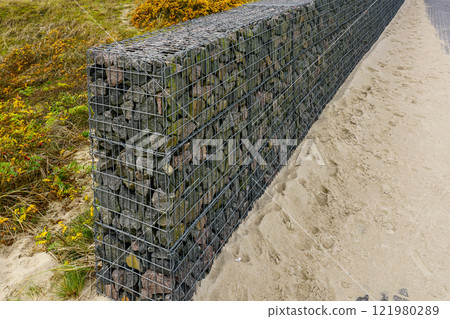 Gabion fence wall from steel mesh filled with granite stones, modern seaside environmental object 121980289