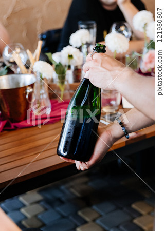 Uncorking a chilled champagne bottle at an elegant celebration, surrounded by floral decor 121980807