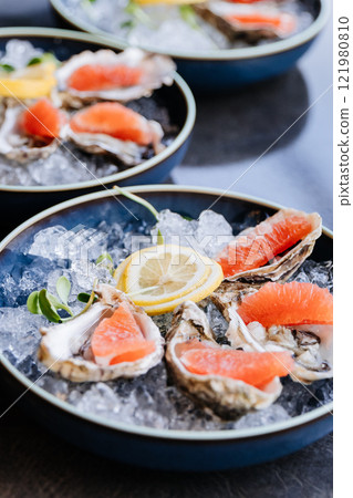 Fresh oysters on ice with grapefruit slices and lemon garnish for a gourmet dining experience Fresh oysters on ice with grapefruit slices and lemon garnish for a gourmet dining experience 121980810