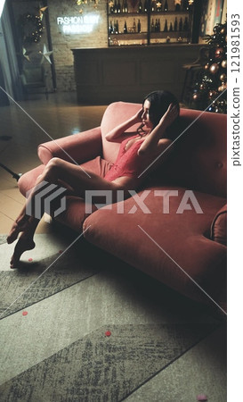 Beautiful brunette posing sexy on camera in red lace bodysuit while sitting on sofa Beautiful brunette posing sexy on camera in red lace bodysuit while sitting on sofa 121981593