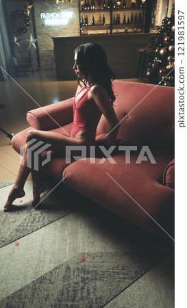 Beautiful brunette posing sexy on camera in red lace bodysuit while sitting on sofa Beautiful brunette posing sexy on camera in red lace bodysuit while sitting on sofa 121981597