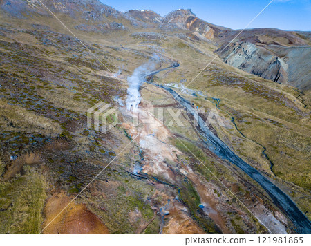 Aerial of the geothermal landscape of Hveragerdi, showcasing a steaming vent surrounded by vibrant moss and a gently flowing stream 121981865