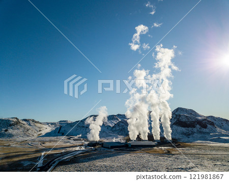 White steam billows from the geothermal power plant in Hellisheidi, Iceland, contrasting with the snowy peaks of Iceland's breathtaking winter scenery in this aerial 121981867