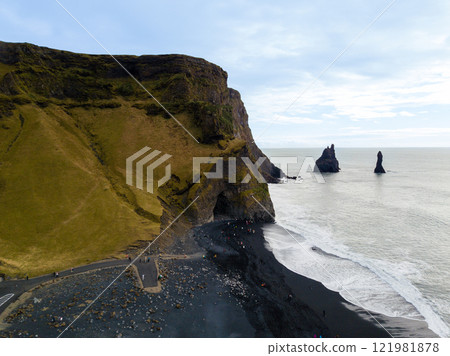 Aerial: Tourists admiring the stunning Reynisdrangar sea stacks from the renowned black sand beach of Reynisfjara create a picturesque scene filled with natural beauty Aerial: Tourists admiring the stunning Reynisdrangar sea stacks from the renowned black sand beach of Reynisfjara create a picturesque scene filled with natural beauty 121981878