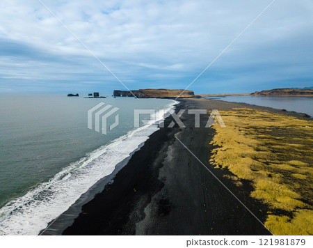 Ocean waves crashing against Reynisfjara, a renowned black sand beach located on Iceland's stunning south coast. The rhythmic motion captivates with its natural beauty and power in this aerial 121981879