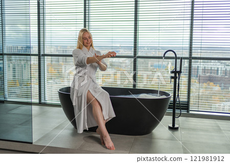 Woman applying moisturizing body lotion on hand arm relaxing in bathroom. Girl rubbing nourishing cream doing daily skincare routine spending morning in bathroom. Beauty treatment spa body skin care Woman applying moisturizing body lotion on hand arm relaxing in bathroom. Girl rubbing nourishing cream doing daily skincare routine spending morning in bathroom. Beauty treatment spa body skin care 121981912
