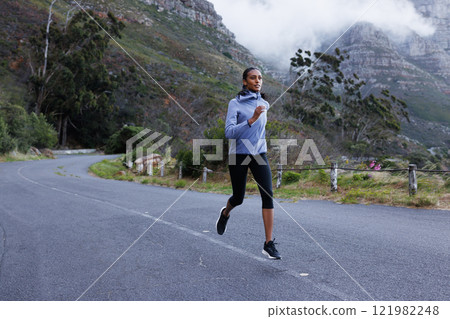 Full length of a slim female athlete running on an abandoned road. Woman in fitness attire jogging on the road in the mountains. Full length of a slim female athlete running on an abandoned road. Woman in fitness attire jogging on the road in the mountains. 121982248