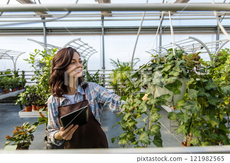 Young dark-haired woman working in a glasshouse checking plants condition 121982565