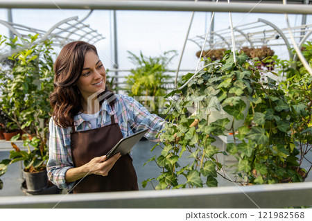 Young dark-haired woman working in a glasshouse checking plants condition Young dark-haired woman working in a glasshouse checking plants condition 121982568