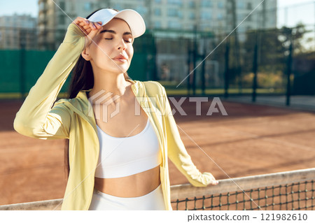 Cute female tennis player in white cap feeling happy and smiling Cute female tennis player in white cap feeling happy and smiling 121982610