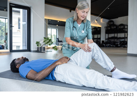 Female physical therapist helping her male patient in rehabilitation exercising for legs 121982623