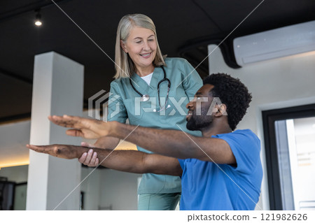 Young male patient exercising with physical therapist and stretching his arms 121982626