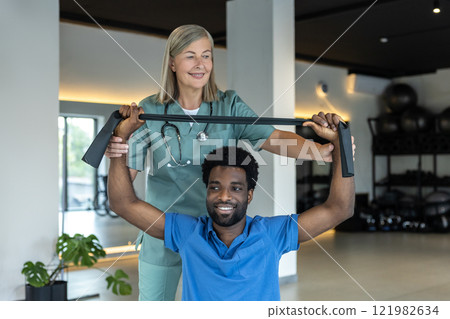 Young african american man exercising with a stretch band during rehabilitation session Young african american man exercising with a stretch band during rehabilitation session 121982634