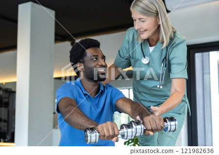 Young male patient exercising with dumbbells with a physical therapist Young male patient exercising with dumbbells with a physical therapist 121982636