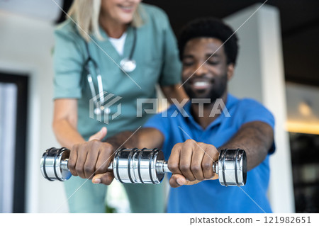 African american young man working on his arms , female doctor guiding him African american young man working on his arms , female doctor guiding him 121982651