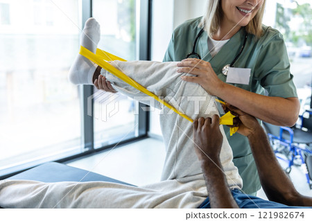 Female doctor helping a male patient during exercising with stretch band 121982674