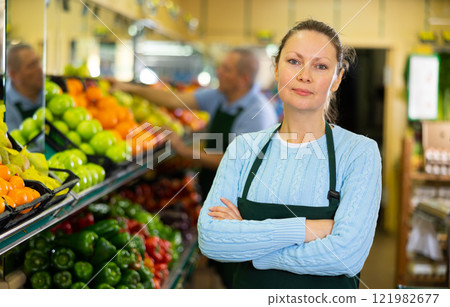 Middle-aged saleswoman standing in front of counter in grocery store 121982677