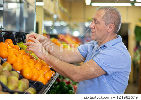 Elderly man purchaser taking fresh tangerines in grocery store 121982679