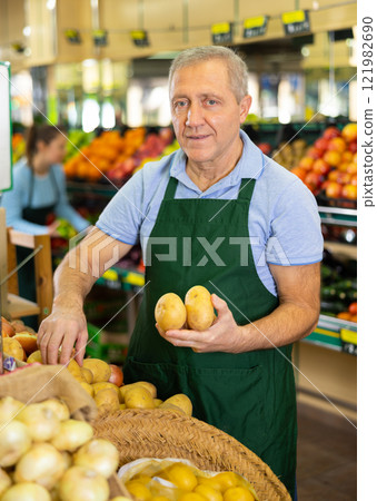 Aged salesman putting potatoes on food stall in greengrocery 121982690
